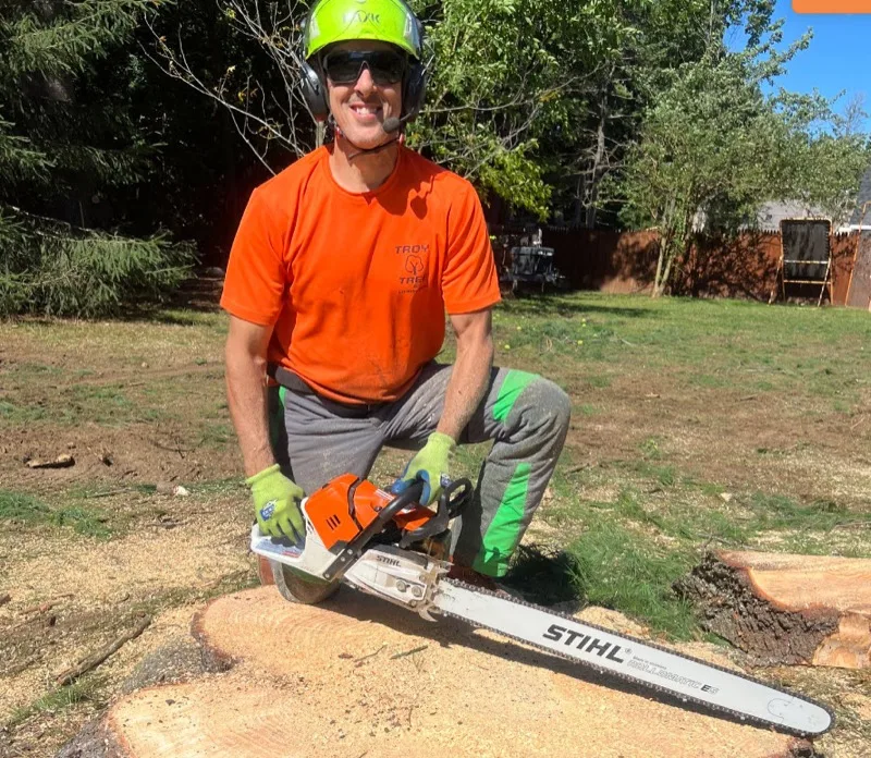 Bobby Troy, founder of Troy Tree and Landscaping, kneeling beside a freshly cut stump with a chainsaw