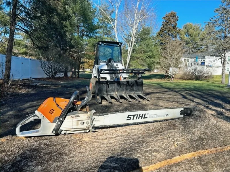 Bobcat skid steer with brush grapple attachment and a Stihl chainsaw on the ground beside it